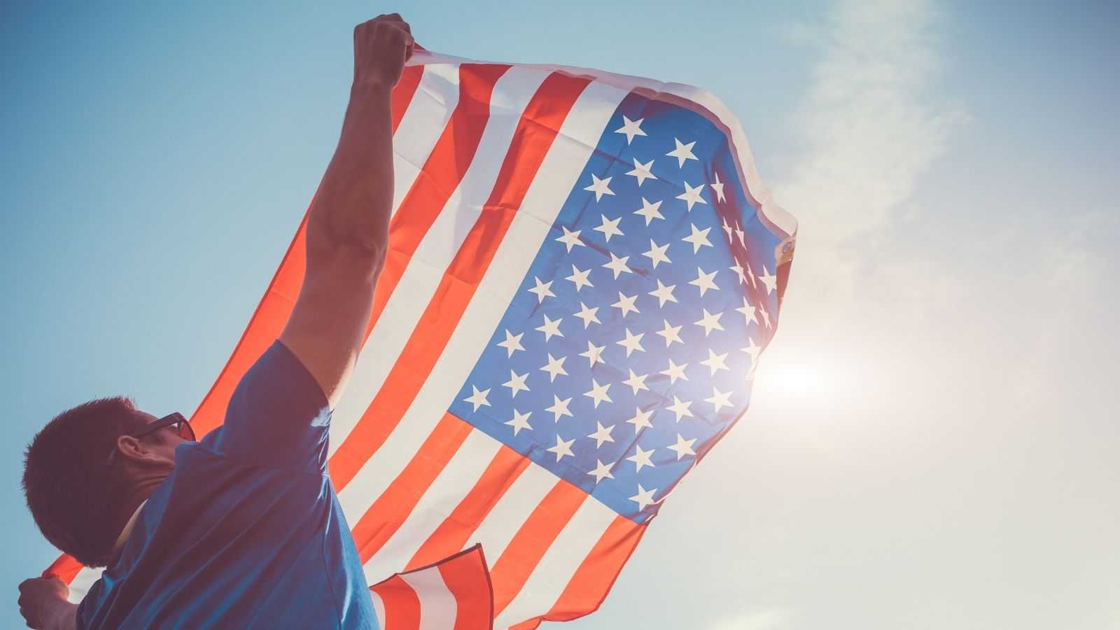 A person holding the American flag towards the sun
